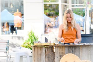 A woman engaged in crafting activities at an outdoor market stall during the day.