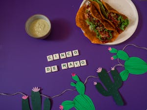 Colorful Cinco de Mayo setup with tacos and cacti decorations on purple background.
