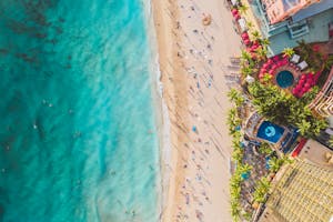 Stunning aerial view of a vibrant beach with people, palm trees, and luxury resorts.
