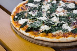 Close-up of a vegetarian pizza topped with ricotta cheese and spinach, served on a wooden board.